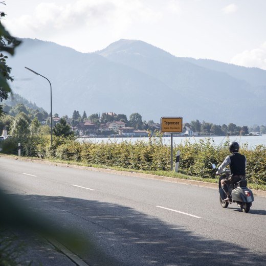 Rollerfahrer passiert die Ortseinfahrt der Stadt Tegernsee, im Hintergrund sieht man den Tegernsee., © Der Tegernsee, Hansi Heckmair