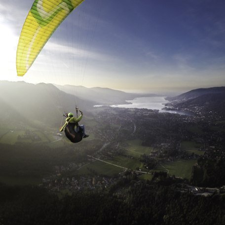 Ein Gleitschirmflieger mit gelbem Schirm fliegt bei untergehender Sonne Richtung Tegernsee, © Dietmar Denger