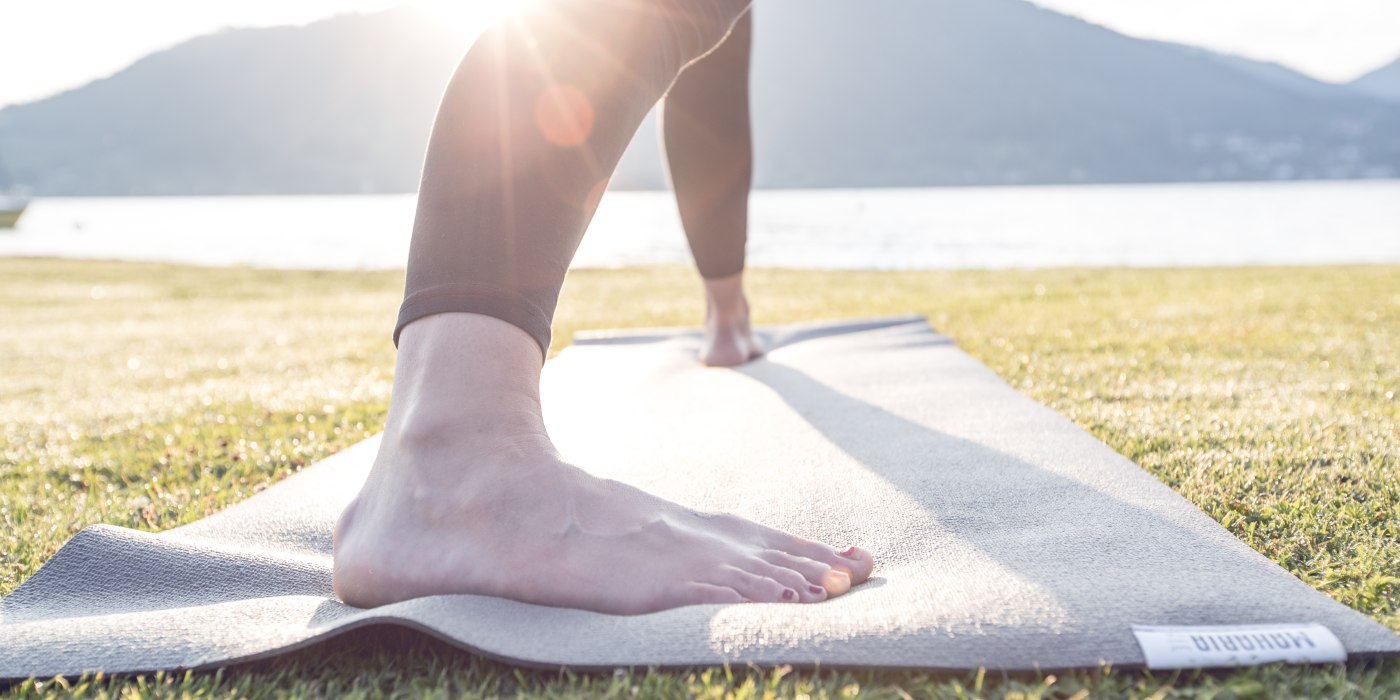 Die Sonne spitzt über die Berge und die Füße stehen fest auf der Matte bei der Yogaübung am Ufer des Tegernsees, © Hansi Heckmair