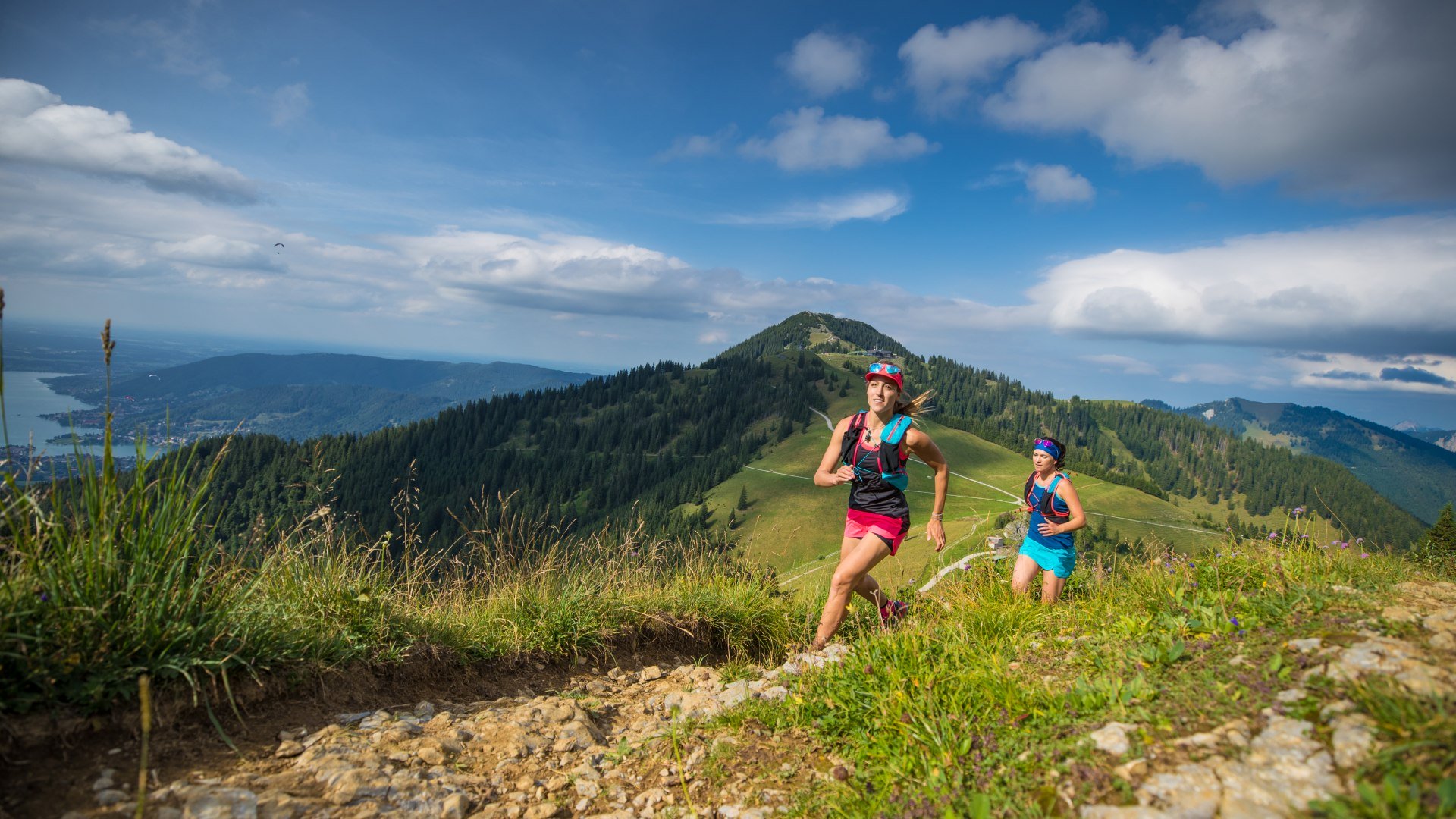 Zwei Trailrunnerinnen laufen auf einem Trail in den Bayerischen Voralpen mit Blick auf den Tegernsee, © Hansi Heckmair