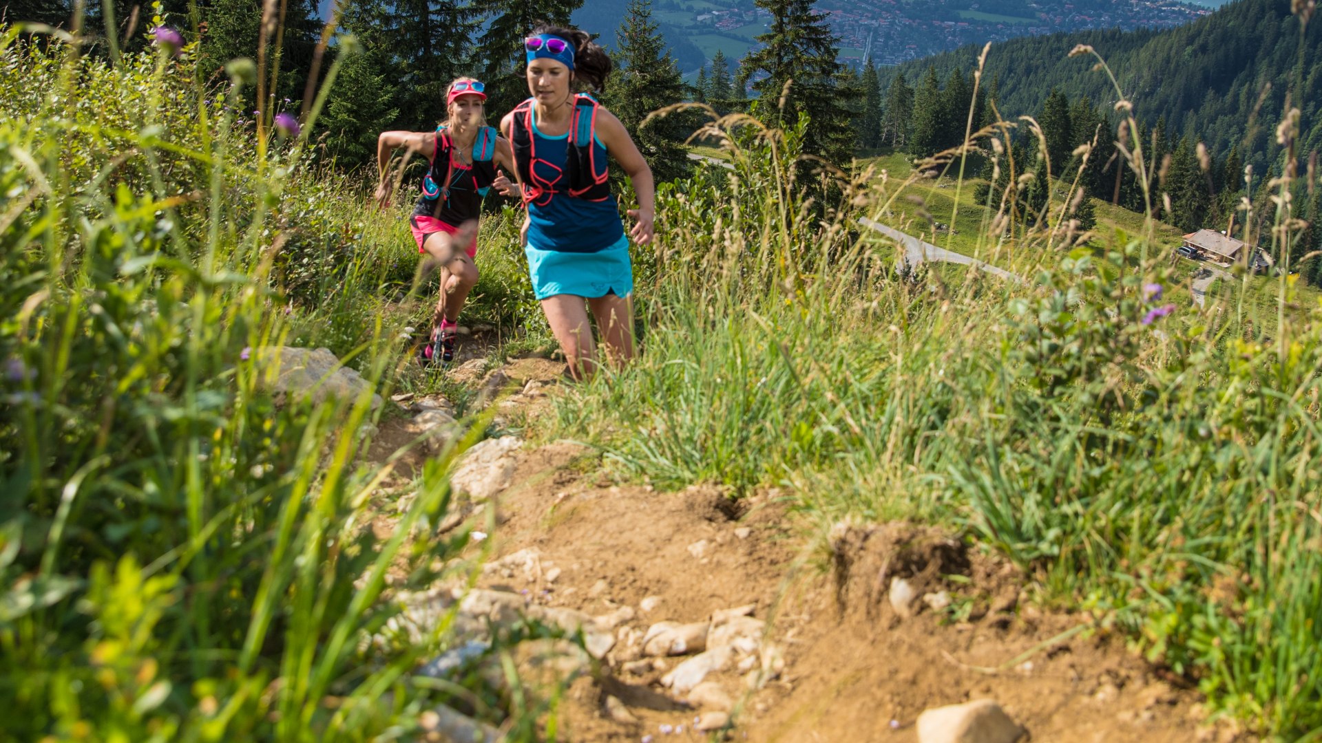 Ein schmaler Trail führt den Berg hinauf im Hintergrund sieht man zwei Läuferinnen und den Tegernsee., © Hansi Heckmair Ein schmaler Trail führt den Berg hinauf im Hintergrund sieht man zwei Läuferinnen und den Tegernsee., © Hansi Heckmair