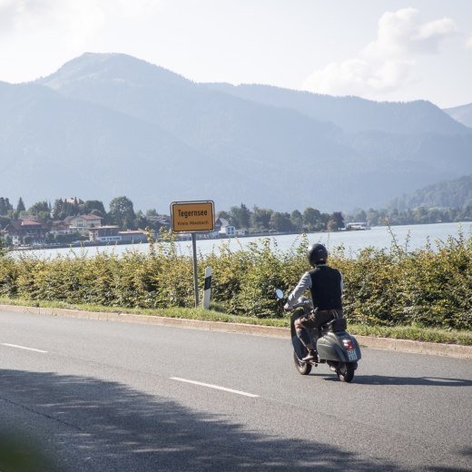 Rollerfahrer passiert die Ortseinfahrt der Stadt Tegernsee, im Hintergrund sieht man den Tegernsee., © Der Tegernsee, Hansi Heckmair