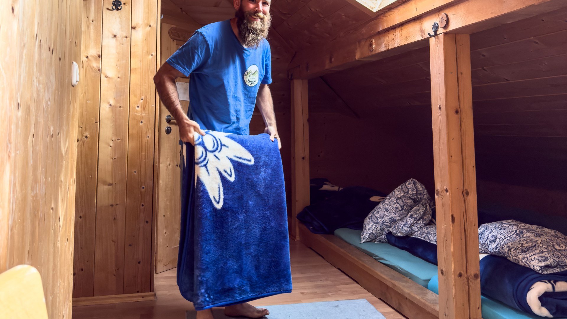 Sebastian Bailey sch&uuml;ttelt die  neuen Flauschedecken auf im Matratzenlager der Tegernseer H&uuml;tte