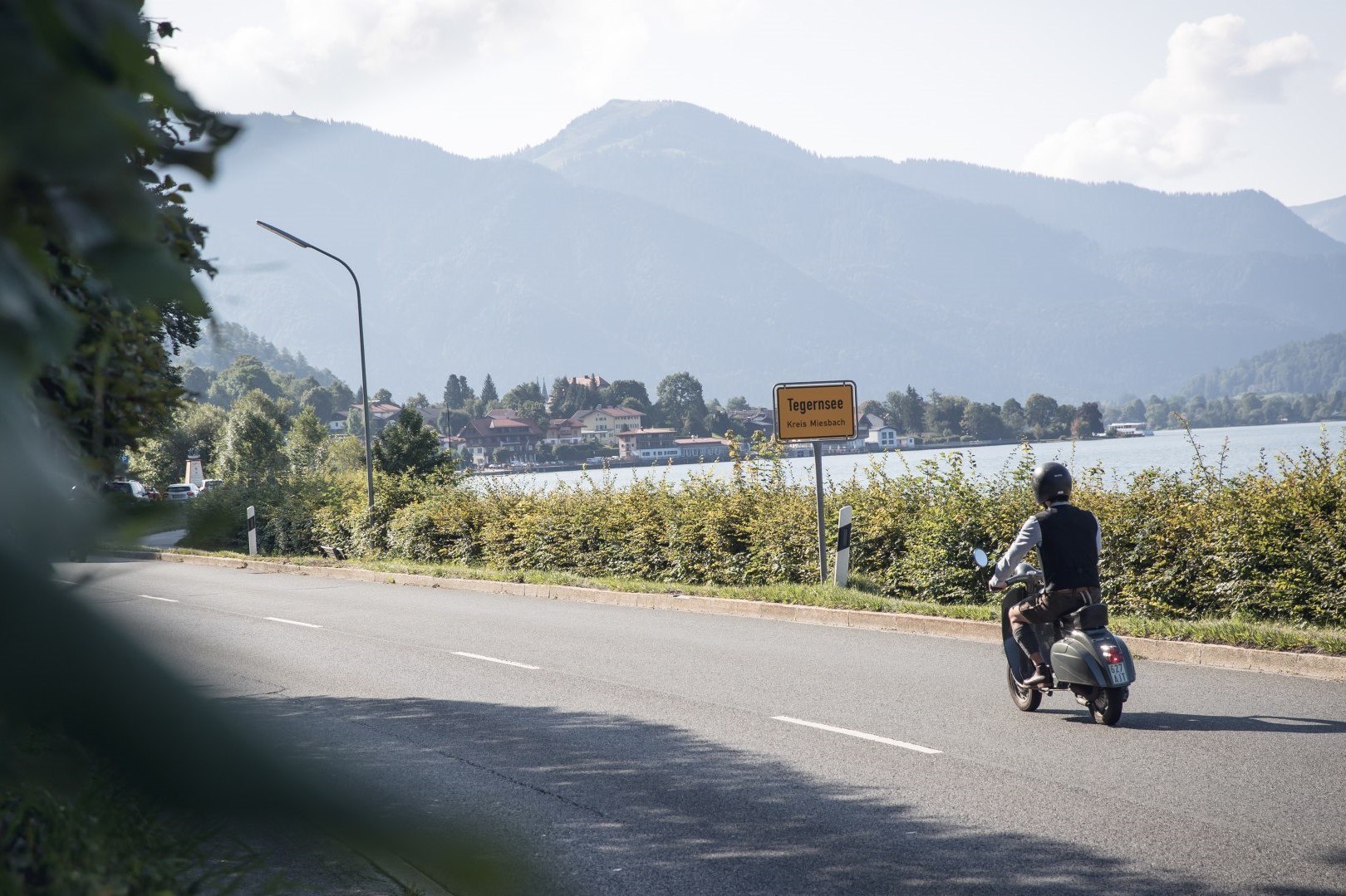 Rollerfahrer passiert die Ortseinfahrt der Stadt Tegernsee, im Hintergrund sieht man den Tegernsee., © Der Tegernsee, Hansi Heckmair