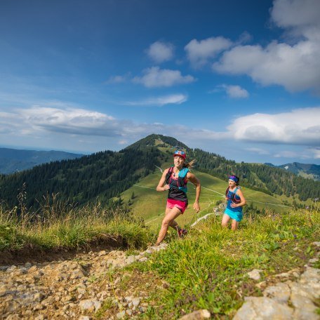 Zwei Trailrunnerinnen laufen auf einem Trail in den Bayerischen Voralpen mit Blick auf den Tegernsee, © Hansi Heckmair Zwei Trailrunnerinnen laufen auf einem Trail in den Bayerischen Voralpen mit Blick auf den Tegernsee, © Hansi Heckmair