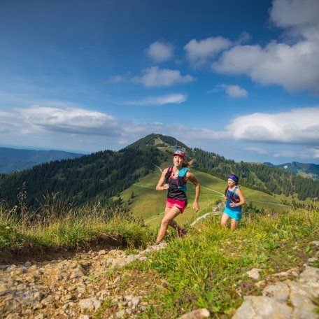 Zwei Trailrunnerinnen laufen auf einem Trail in den Bayerischen Voralpen mit Blick auf den Tegernsee, © Hansi Heckmair